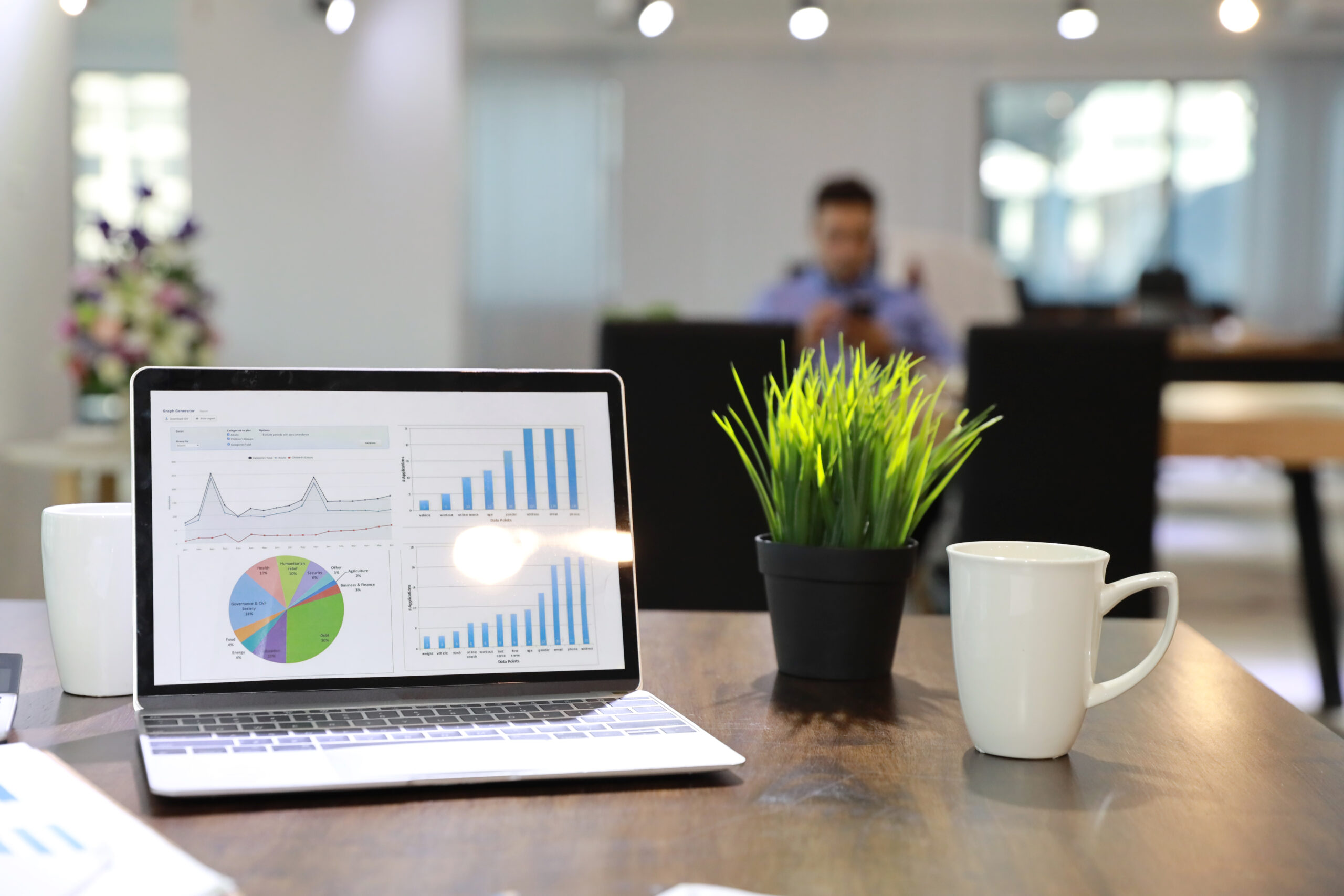 modern office with computer on wood desk, office supplies and coffee cup with business people blurred background