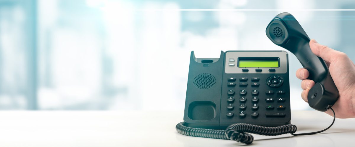 Dialing landline telephone keypad concept for communication, contact us and customer service support. hand holding voip telephone receiver on blurred office background. banner