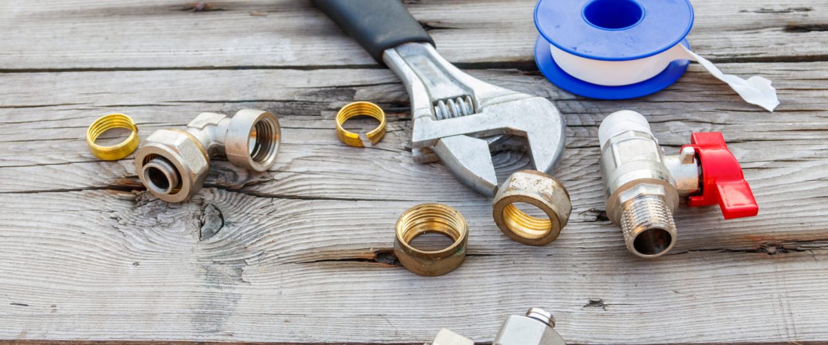 Various plumbing spare parts, sealing tape and adjustable wrench on rustic wooden background